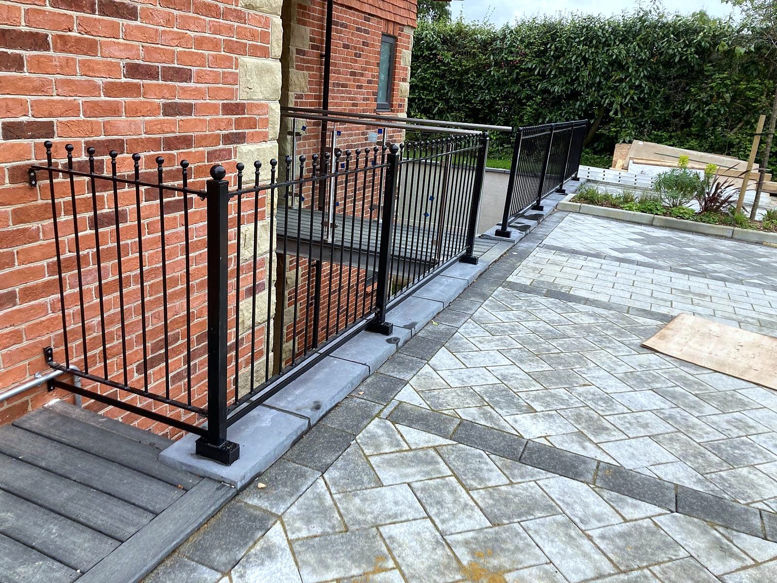 Black finial railings and post railings around a paved area of a red brick building