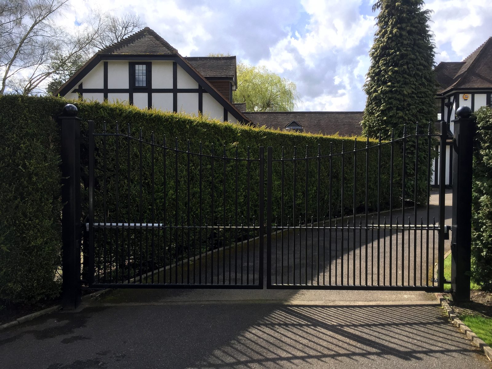 Black steel double driveway gates hung on steel posts between hedges