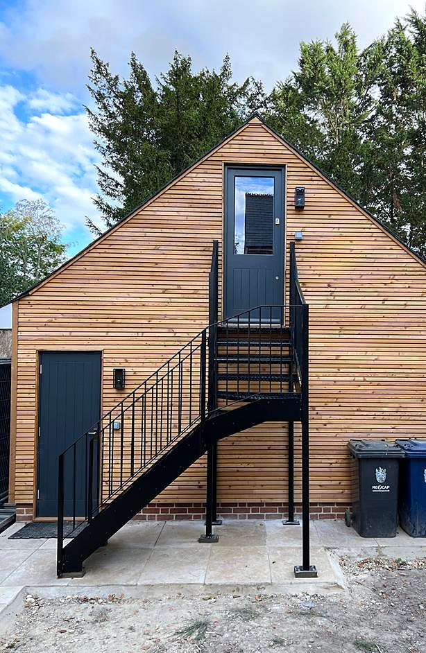 Black steel external staircase and landing up to the door of a timber-clad garden building