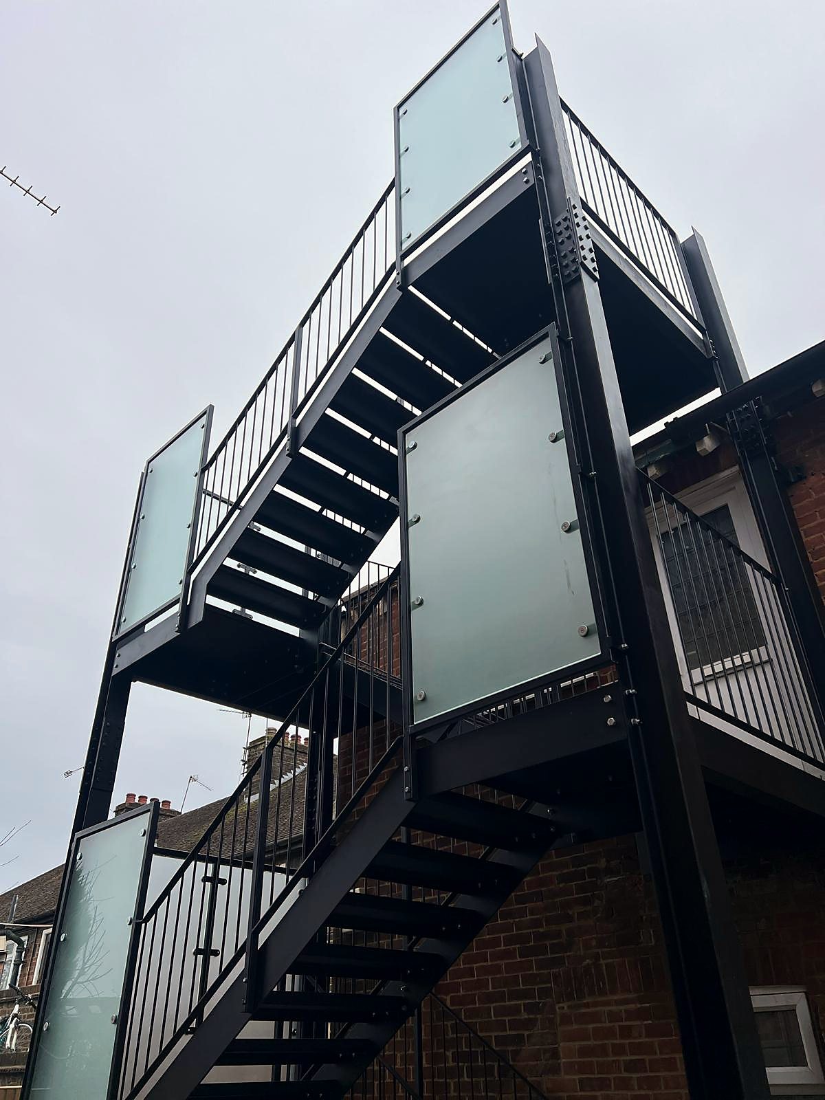 Black steel multi-level external staircase with frosted glass privacy panels on the landings