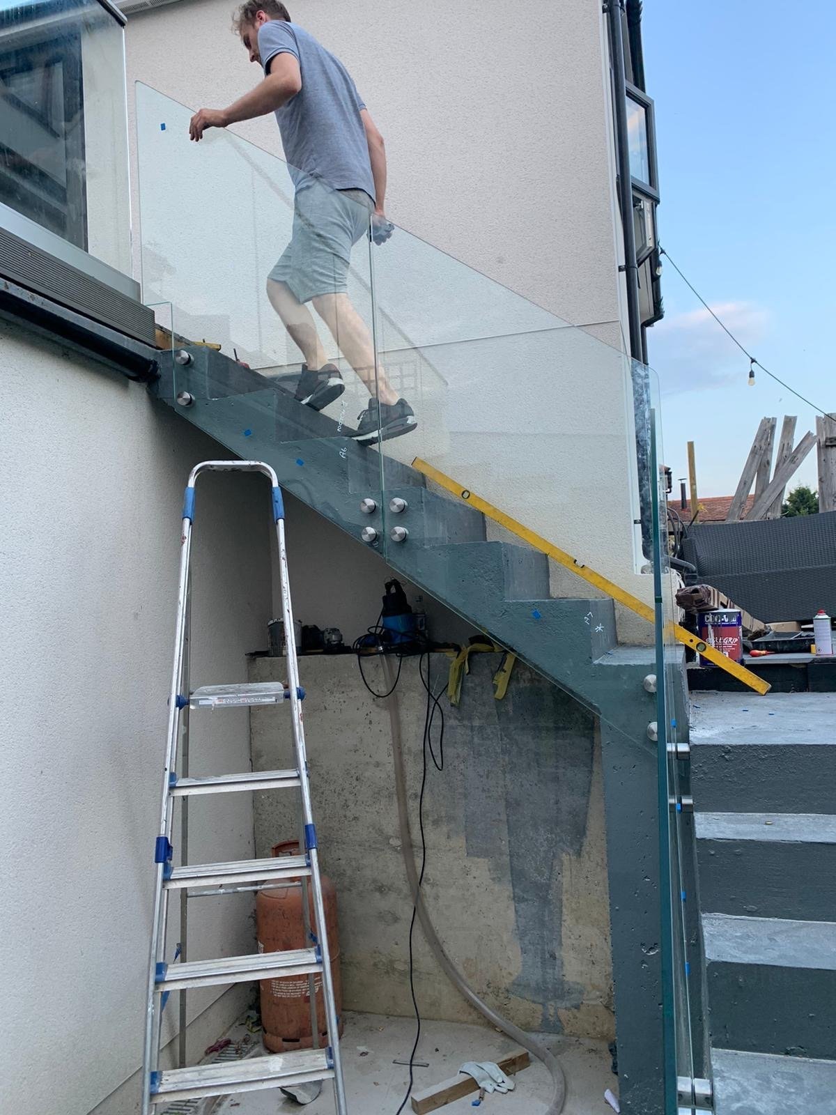 Fitter installing an external steel staircase with frameless glass balustrade