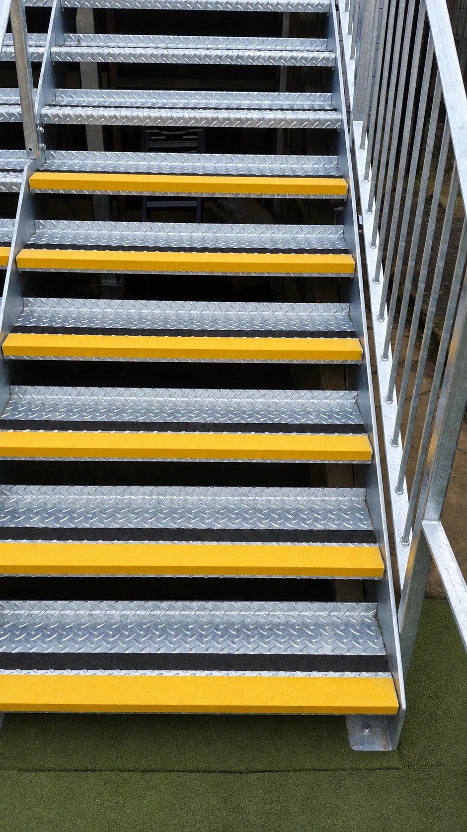 Close view of galvanised chequer-plate treads with yellow anti-slip nosings and a bar balustrade
