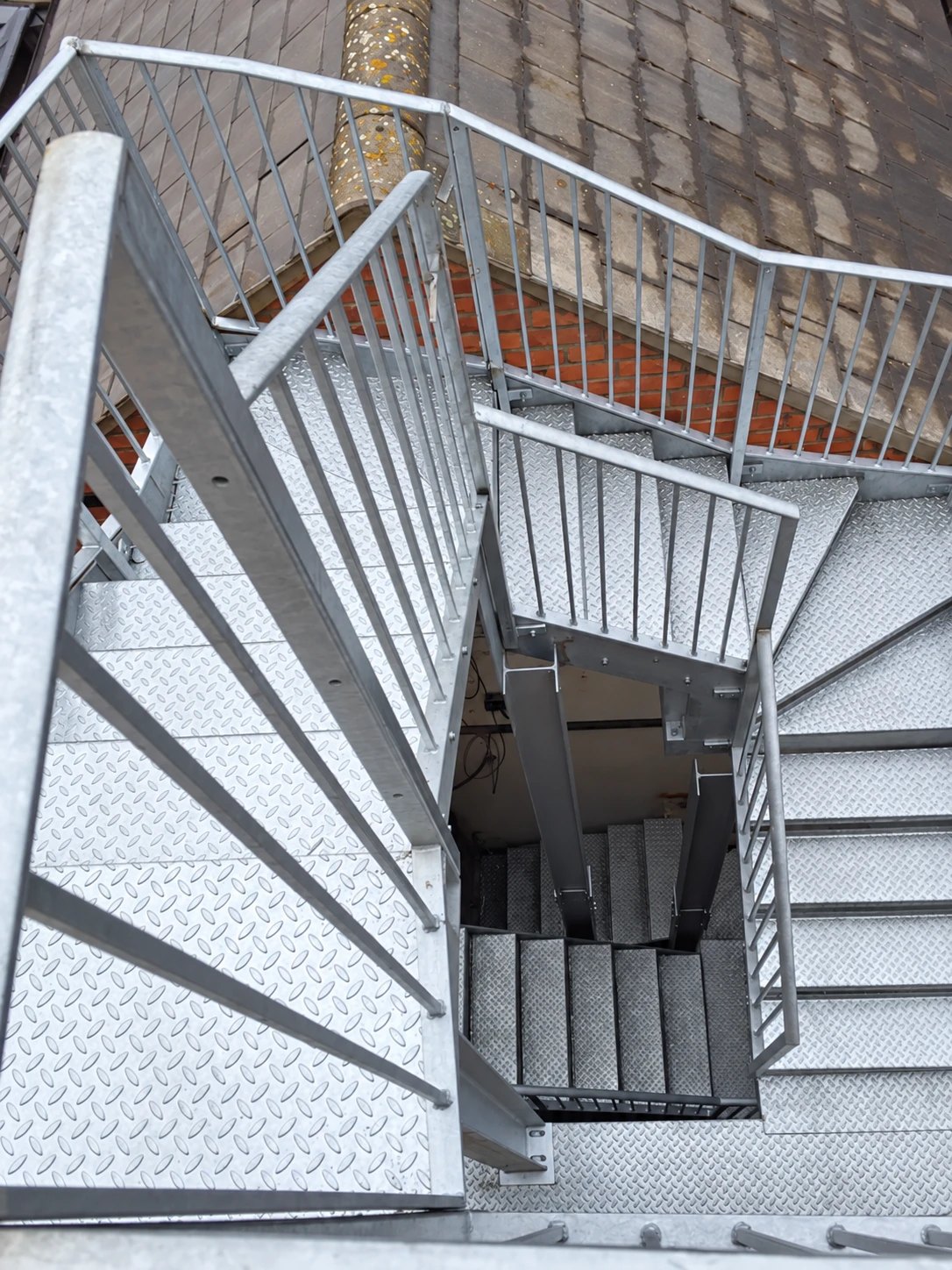 Looking down a multi-flight galvanised steel staircase with chequer-plate treads, landings and bar balustrades