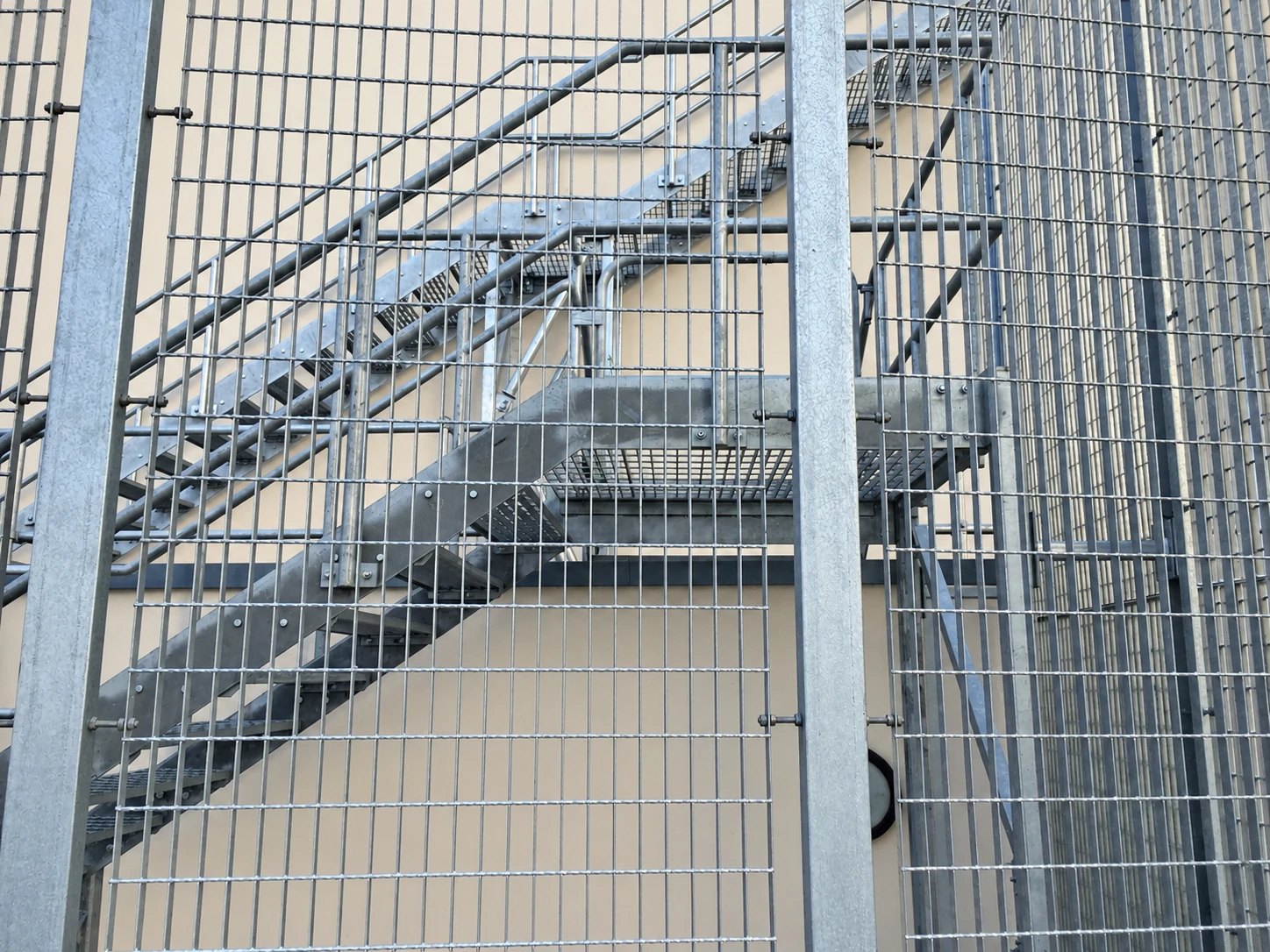 Galvanised steel stair flights and a grating landing seen through the mesh panels of a stair tower