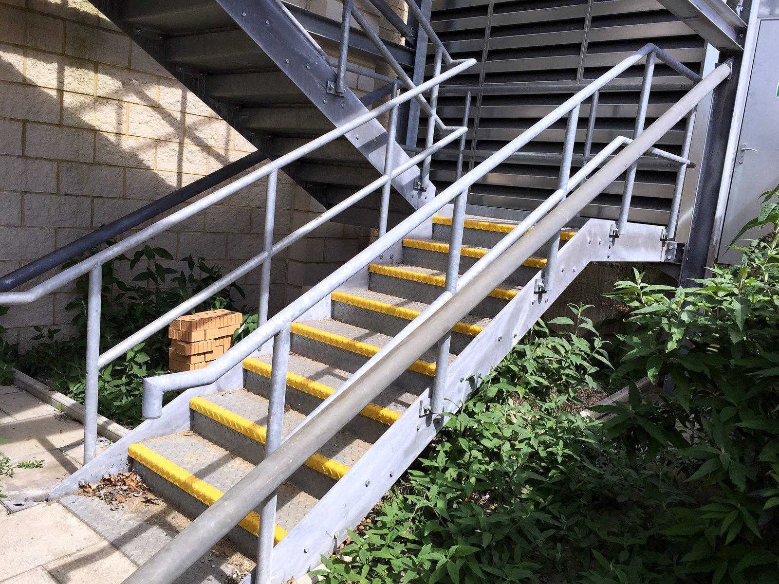 Galvanised stair with yellow anti-slip nosings and twin tube handrails outside a commercial building