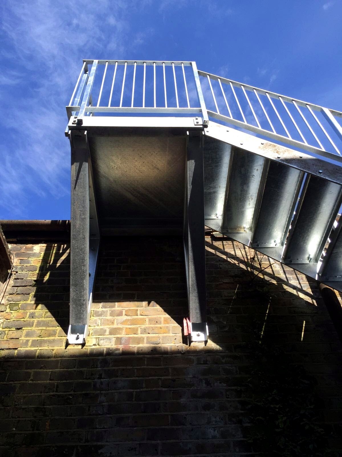Galvanised steel landing on posts with a stair flight above, seen from below