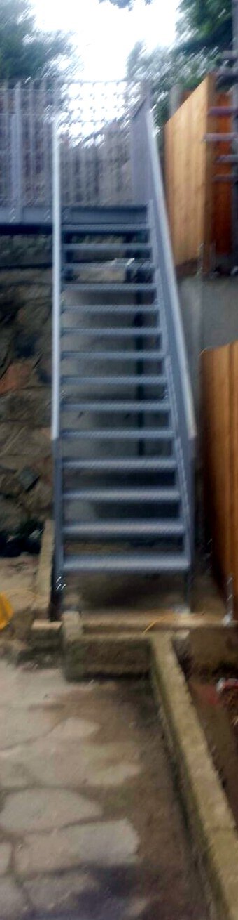 Galvanised steel stair at the end of a paved side passage leading up to a raised level