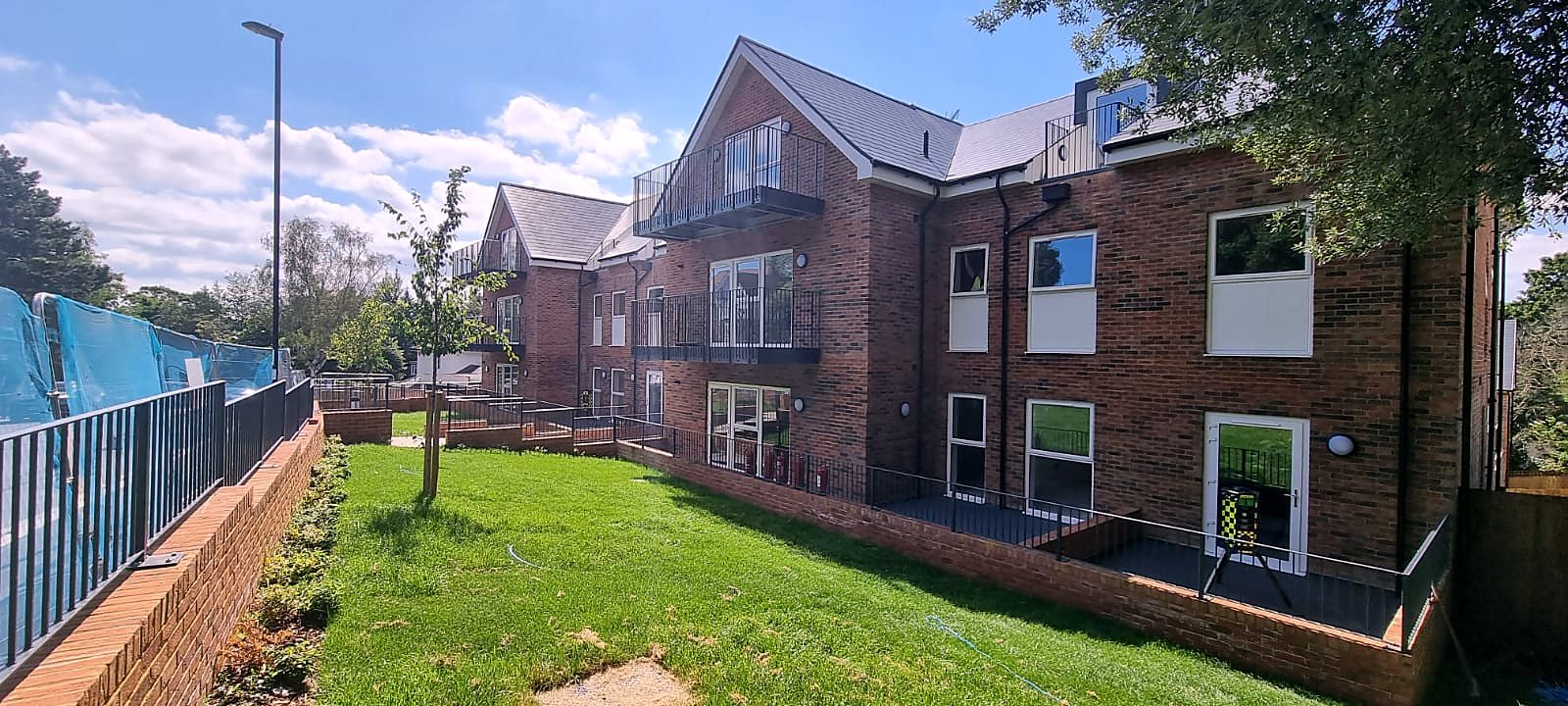 Steel balconies on the back of new brick flats, seen across the lawn